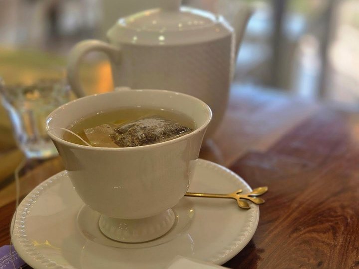 Una taza de té en porcelana blanca con su tetera, sobre una mesa de madera